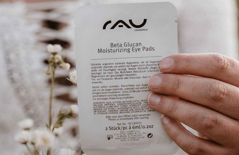 DSC_1e125-02 Die Verpackung der RAU Cosmetics Beta Glucan Moisturizing Eye Pads wird von einer Person gehalten und hebt die hautpflegenden Vorteile von Beta Glucan hinsichtlich der Feuchtigkeitsversorgung und des Hautschutzes hervor.